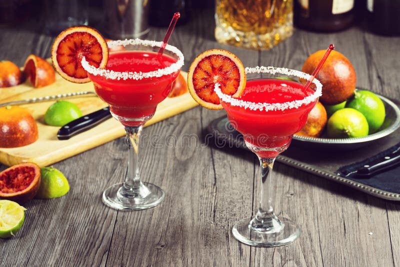 Two blood orange margaritas with salted rims have been made in a vintage-style bar. The ingredients are in the background. Two blood orange margaritas with salted rims have been made in a vintage-style bar. The ingredients are in the background.