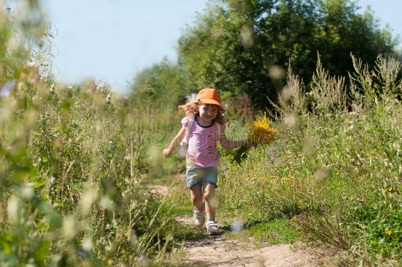 Bloeit het een weinig glimlachende meisje met een boeket van de gebiedszomer het lopen langs de weg van een bos stock foto Bloeit het een weinig glimlachende meisje met een boeket van de gebiedszomer het lopen langs de weg van een bos stock foto