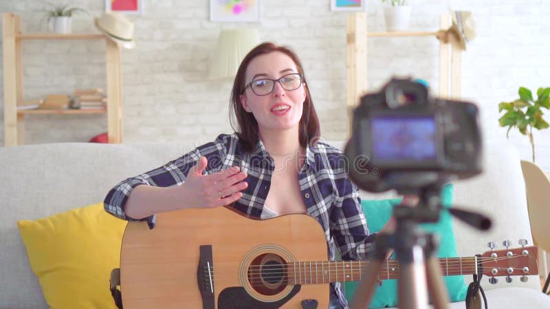Blogger de jeune femme de portrait s'asseyant sur le divan avec une guitare dans des ses mains devant la caméra MOIS lent banque de vidéos