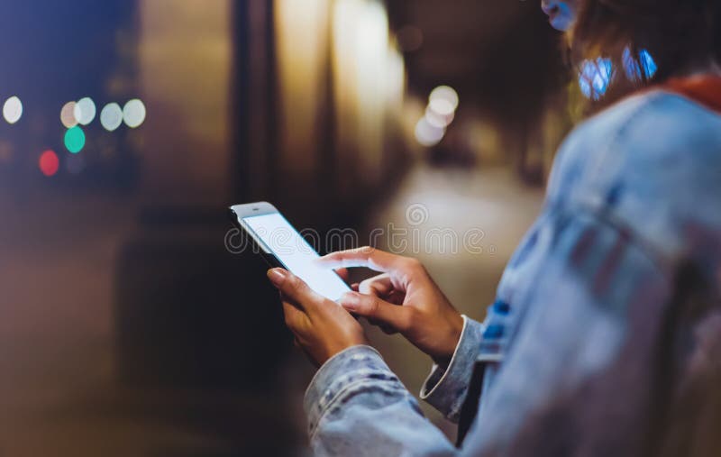 Lumbar en manos móvil teléfono, una mujer mochila muestra dedo sobre el vacío pantalla sobre el la luz en noche atmosférico la ciudad, calles, conectado a red informática mundial.