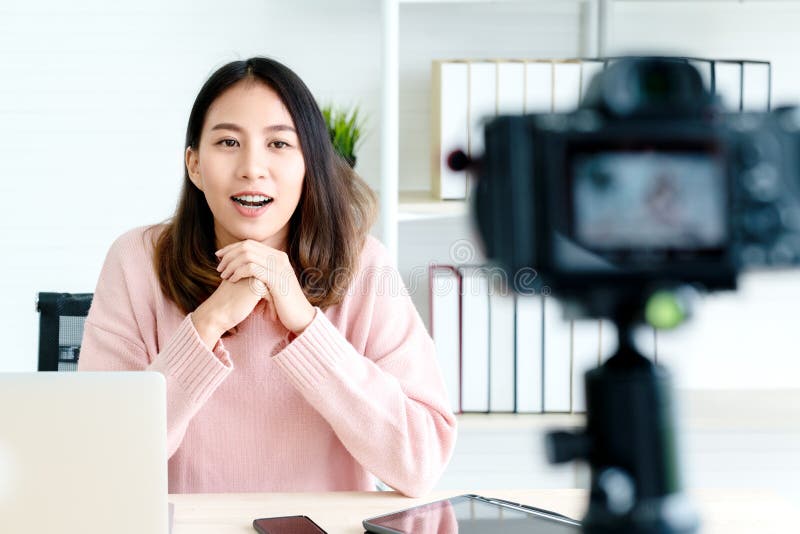 Blogger o vlogger asi?tico atractivo joven de la mujer que mira la c?mara y que habla en el tiroteo video con tecnolog?a Media so fotos de archivo Blogger o vlogger asi?tico atractivo joven de la mujer que mira la c?mara y que habla en el tiroteo video con tecnolog?a Media so fotos de archivo