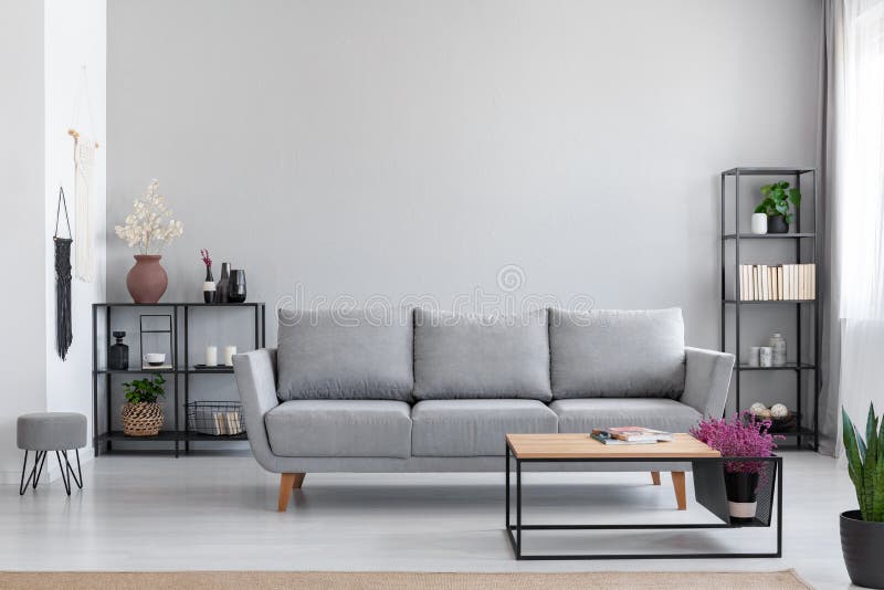 Blommor i trätabellen som är främst av grå soffa i den moderna enkla lägenheten som är inre med stolen arkivbild