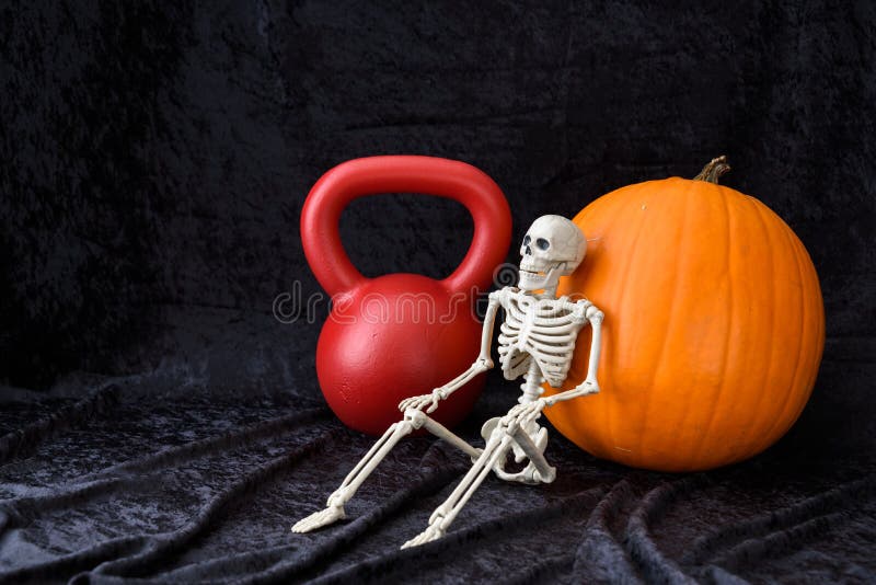 Blomsterhet, orange pumpa, rödkettlebell och vitt skelett på svart sammetsbakgrund royaltyfria bilder