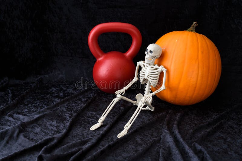 Blomsterhet, orange pumpa, rödkettlebell och vitt skelett på svart sammetsbakgrund royaltyfri foto