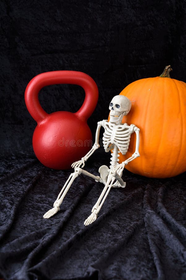 Blomsterhet, orange pumpa, rödkettlebell och vitt skelett på svart sammetsbakgrund royaltyfria bilder