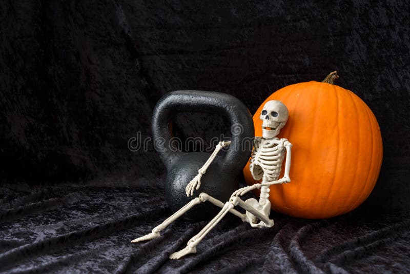 Blomsterhet, orange pumpa, svart kettlebell och vitt skelett på svart sammetsbakgrund arkivfoto