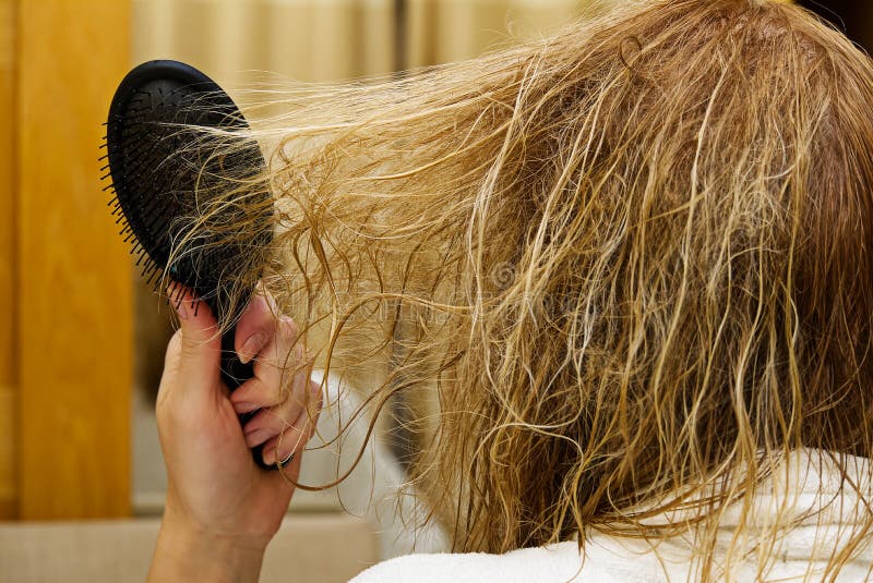 Blond combing wet and tangled hair. Young woman combing her tangled hair after shower, close-up