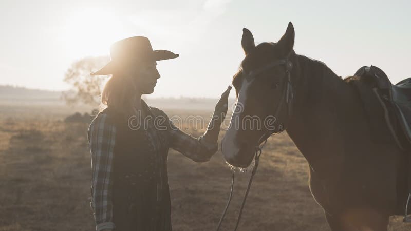 Blond flicka i cowboyhatt som slår och kramar hästen härlig hästkvinna