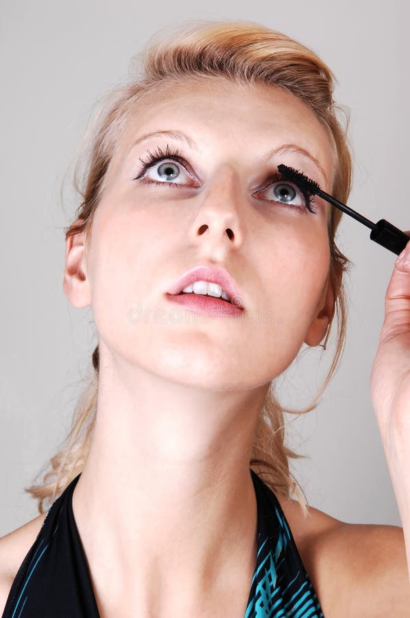 Blond girl fixing her eyelashes.