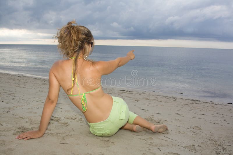 Blond girl pointing to the sea on sunset