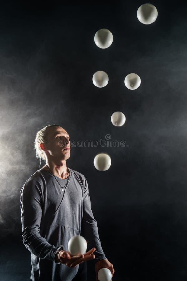 Blond juggler with white balls on black background