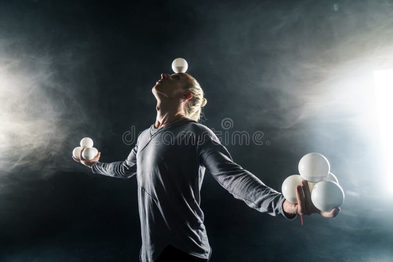 Blond juggler with white balls on black background