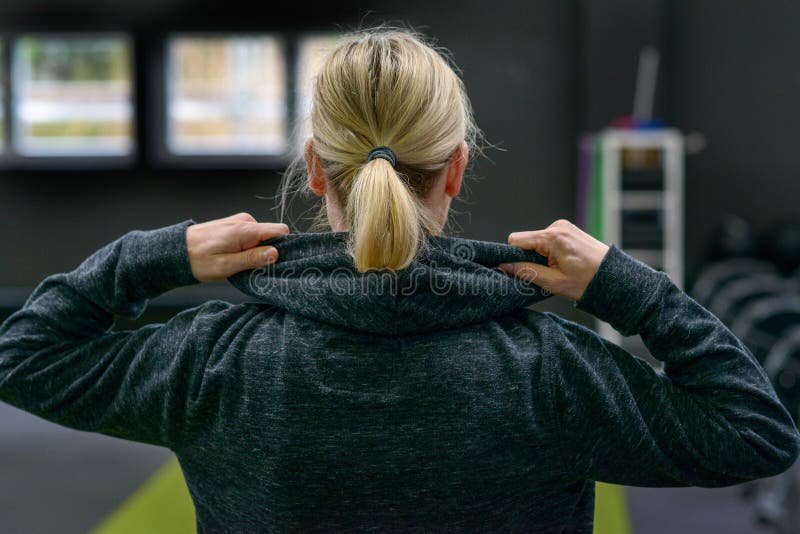 Blond kobieta podnosi kapiszon wierzchołek. Blond kobiety podnosi kapiszon wierzchołek gdy stoi okładzinowego w gym w zakończeniu w górę kierowniczego i ramion widoku daleko od