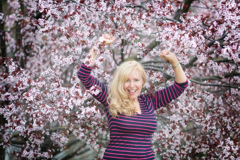 Blond long hair Caucasian woman happy and laughing near blossoming tree stock photo Blond long hair Caucasian woman happy and laughing near blossoming tree stock photo