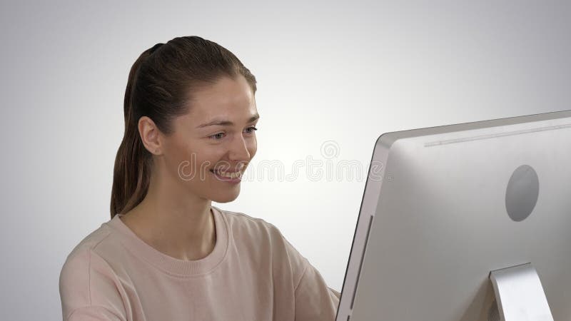 Blond meisje van leerling die de monitor van de computer bekijkt en glimlacht op gradiëntachtergrond