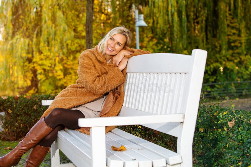 Blond Vrouw Op Een Bank In Het Park En Geniet Van De Herfstzon Stock Afbeelding Image Of