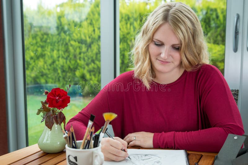 Blond female artist drawing in pencil on the table. Woman in her hobby. Blond female artist drawing in pencil on the table. Woman in her hobby