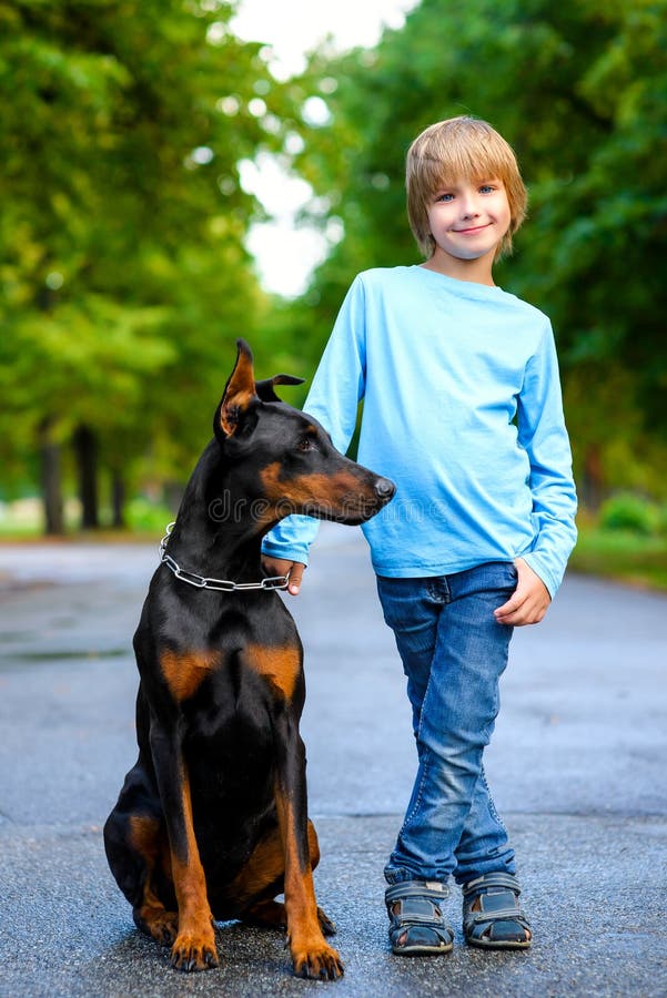 Blonde boy posing with the dog or doberman in