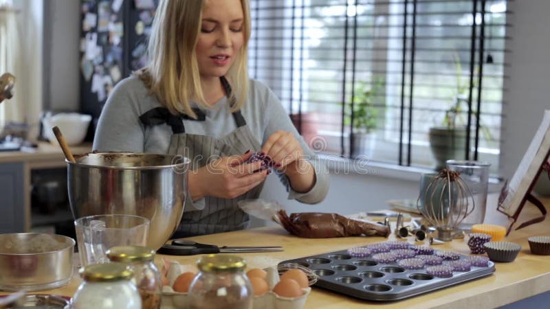 Blonde female putting the wrappers paper cups into the baking dish. Woman cooking cupcakes. Time lapse.