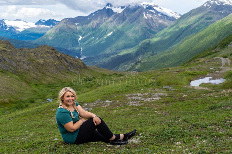 Blonde female sits in the arctic tundra of Alaska on the Trail of 98 along ...