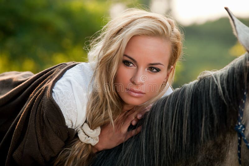 Young blond woman resting on back of horse; countryside background. Young blond woman resting on back of horse; countryside background.