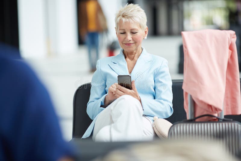 Blonde Frau, die Gerät im Flughafen verwendet stockfotografie Blonde Frau, die Gerät im Flughafen verwendet stockfotografie