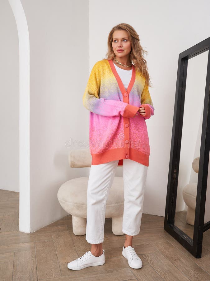 Blonde Frau in farbenfrohen cardigan posiert fröhlich in modernem Innenraum lizenzfreie stockfotografie