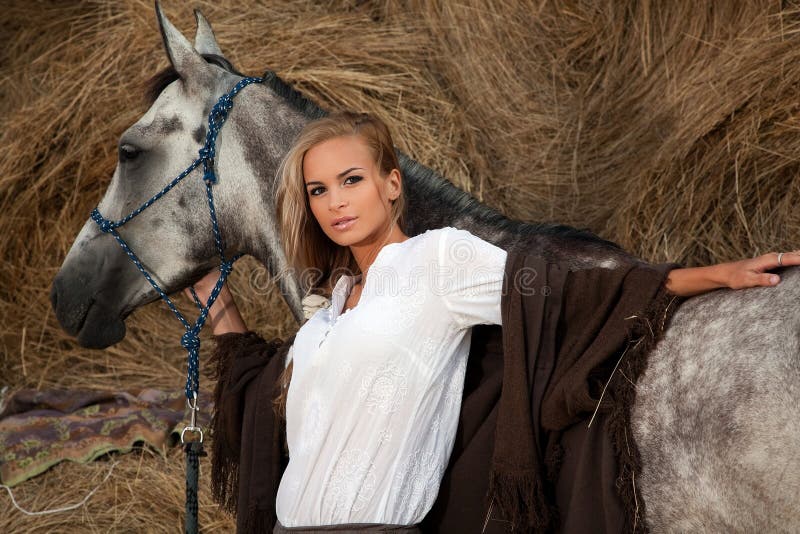 Half body portrait of attractive young blond woman with gray horse; haystack in background. Half body portrait of attractive young blond woman with gray horse; haystack in background.