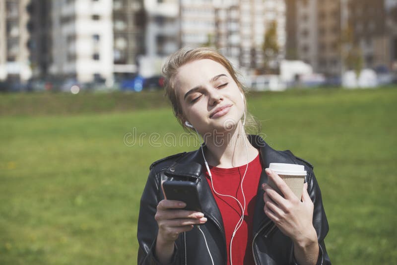Blonde jonge vrouw die lacht naar muziek met een oortelefoon, relaxeert, gebruik makend van smartphone en drink koffie stock foto's Blonde jonge vrouw die lacht naar muziek met een oortelefoon, relaxeert, gebruik makend van smartphone en drink koffie stock foto's