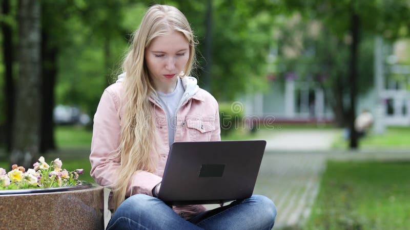 Blonde jonge vrouw werkt op laptop in park