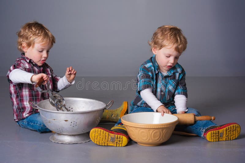 Cute blonde twins playing with cooking bowls and utensils. Cute blonde twins playing with cooking bowls and utensils
