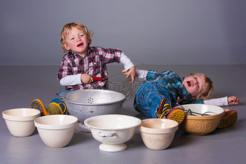 Cute blonde twins fighting over cooking bowls and utensils. Cute blonde twins fighting over cooking bowls and utensils