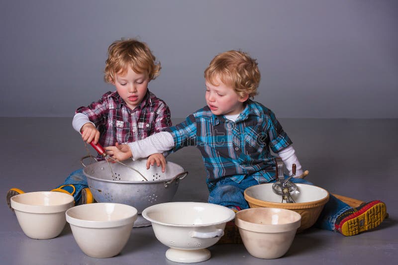 Cute blonde twins squabbling over cooking bowls and utensils. Cute blonde twins squabbling over cooking bowls and utensils