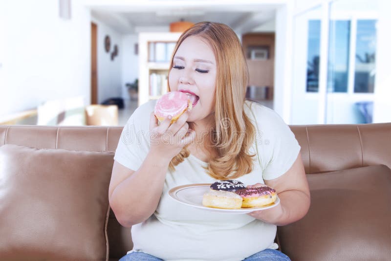 Picture of a blonde obesity woman sitting on the sofa while eating donuts at home. Picture of a blonde obesity woman sitting on the sofa while eating donuts at home