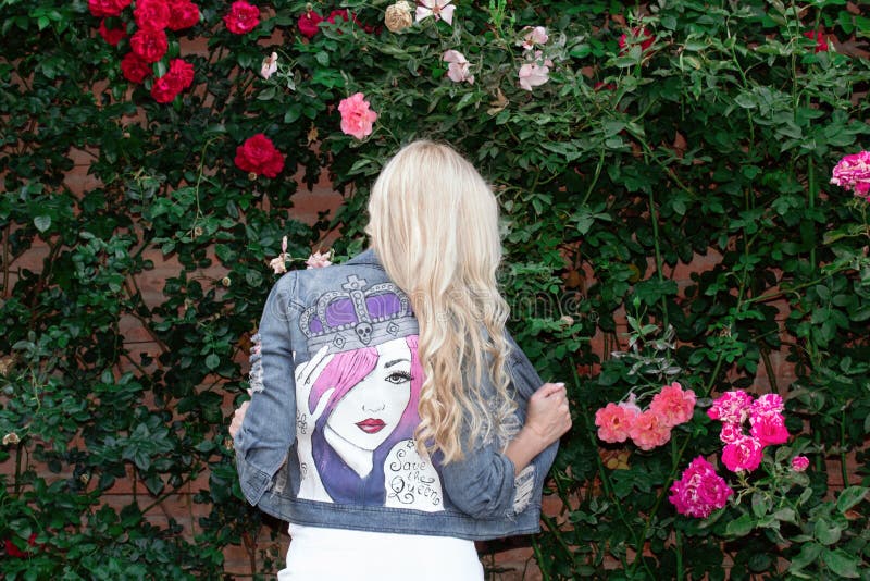 Blonde meisje dat zich in een geschilderd Jean jack op de achtergrond van groen en bloemen poetst royalty-vrije stock afbeeldingen Blonde meisje dat zich in een geschilderd Jean jack op de achtergrond van groen en bloemen poetst royalty-vrije stock afbeeldingen