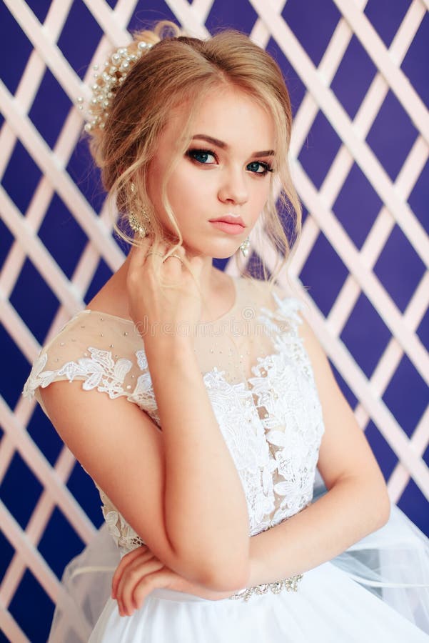 Blonde muy hermoso con los ojos azules en el vestido blanco de la novia en fondo púrpura en estudio fotografía de archivo Blonde muy hermoso con los ojos azules en el vestido blanco de la novia en fondo púrpura en estudio fotografía de archivo