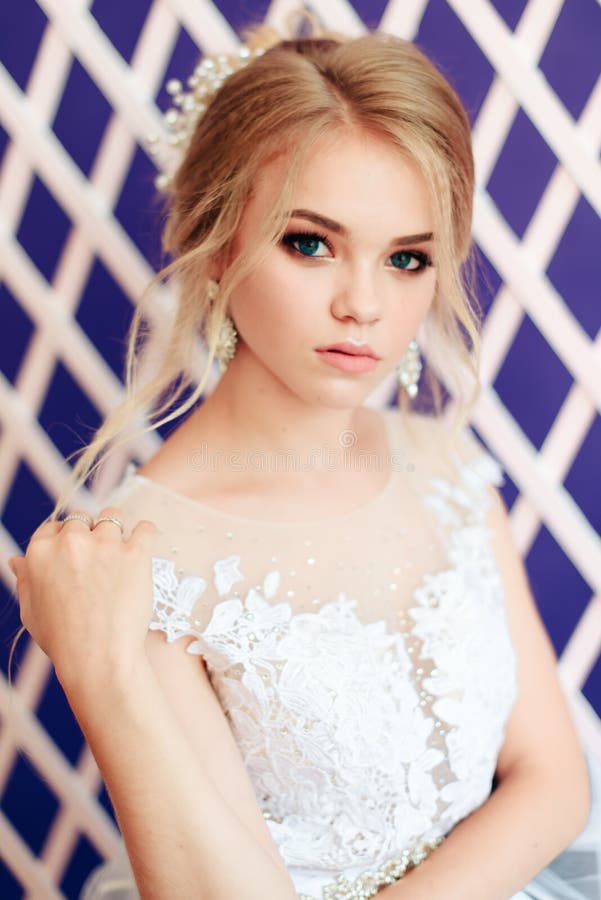 Blonde muy hermoso con los ojos azules en el vestido blanco de la novia en fondo púrpura en estudio imagen de archivo Blonde muy hermoso con los ojos azules en el vestido blanco de la novia en fondo púrpura en estudio imagen de archivo