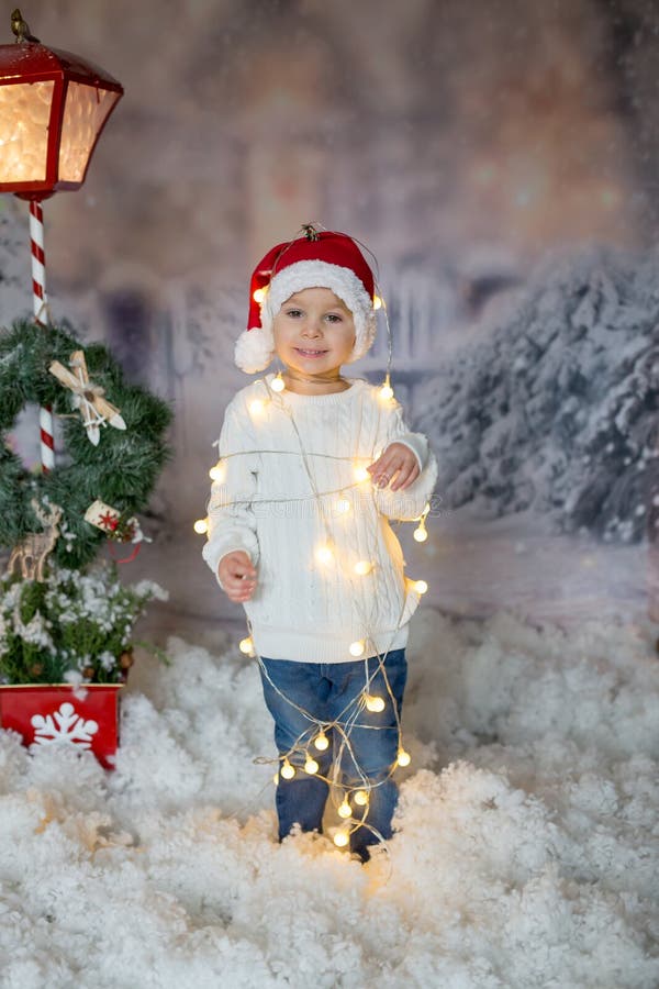 Cute toddler boy, blond child, standing in front of the house, wrapped in christmas string lights, feeling trapped. Cute toddler boy, blond child, standing in front of the house, wrapped in christmas string lights, feeling trapped