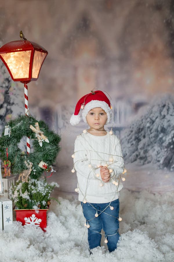 Cute toddler boy, blond child, standing in front of the house, wrapped in christmas string lights, feeling trapped. Cute toddler boy, blond child, standing in front of the house, wrapped in christmas string lights, feeling trapped