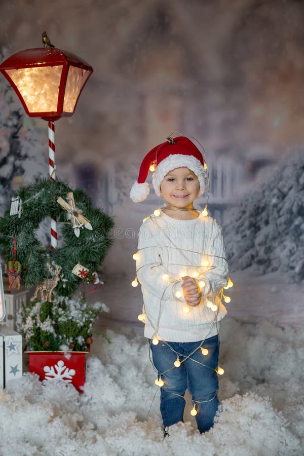 Cute toddler boy, blond child, standing in front of the house, wrapped in christmas string lights, feeling trapped. Cute toddler boy, blond child, standing in front of the house, wrapped in christmas string lights, feeling trapped