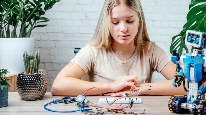 A blonde teen girl plugging cables to sensor chips while learning arduino coding and robotics royalty free stock photos