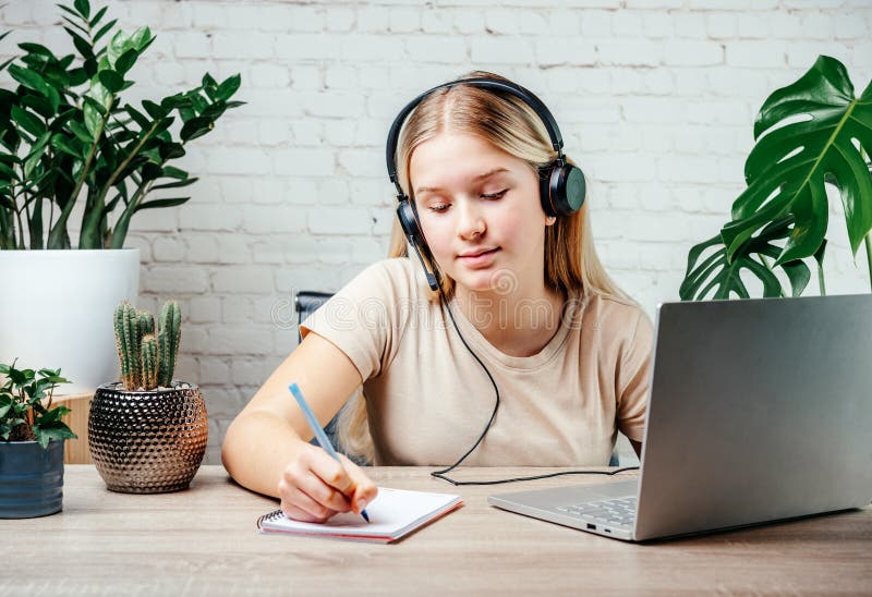 Blonde teen girl wearing headphones studying online with internet chat skype teacher royalty free stock photos