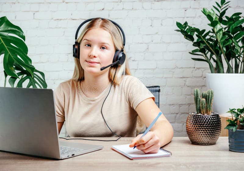 Blonde teen girl wearing headphones studying online with internet chat skype teacher stock photos