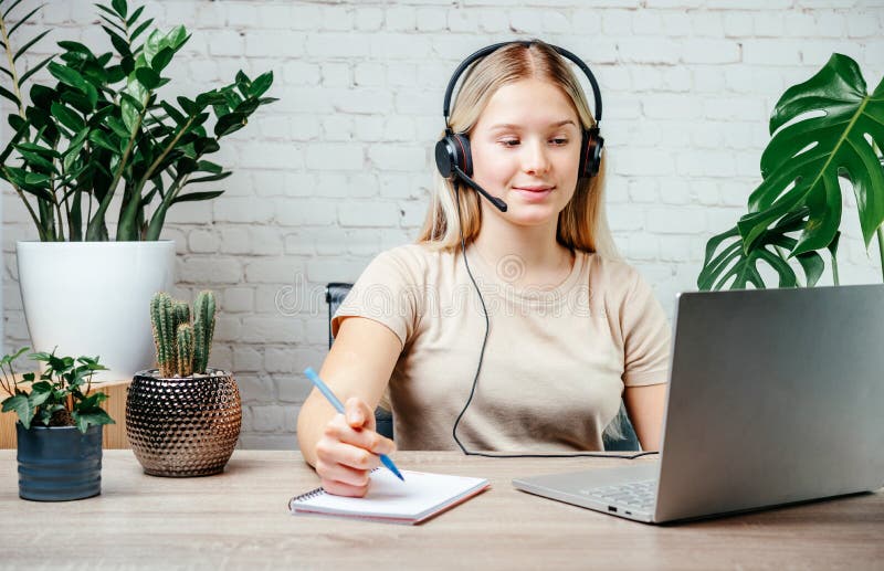 Blonde teen girl wearing headphones studying online with internet chat skype teacher royalty free stock image