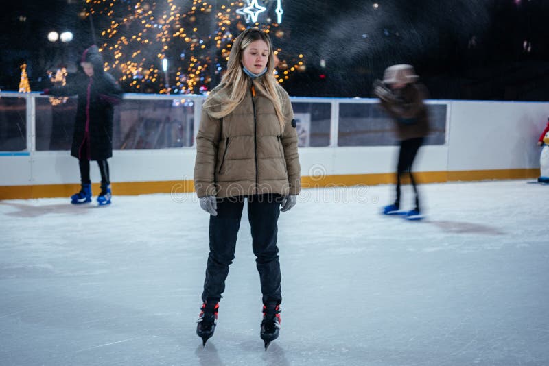 A blonde teenage girl skating on the skating rink with Christmas lights on the background royalty free stock photography