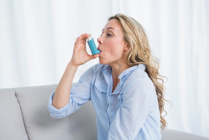 Blonde using her asthma inhaler on couch stock photos Blonde using her asthma inhaler on couch stock photos