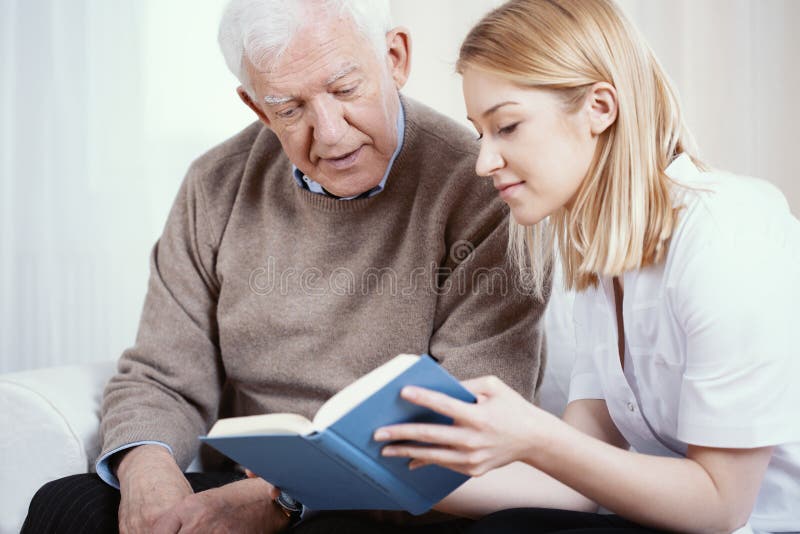 Young blonde volunteer reading book to senior man in nursing home. Young blonde volunteer reading book to senior man in nursing home