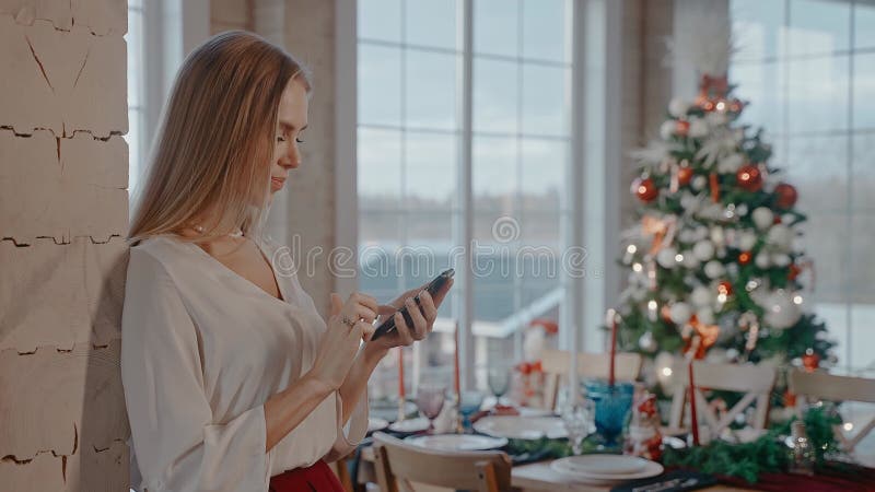 Blonde vrouw sms ' t aan de telefoon voor de eettafel en de kerstboom .