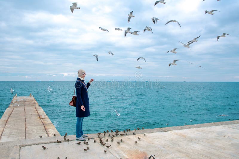 Blonde woman feeding seagulls in cloudy autumn day