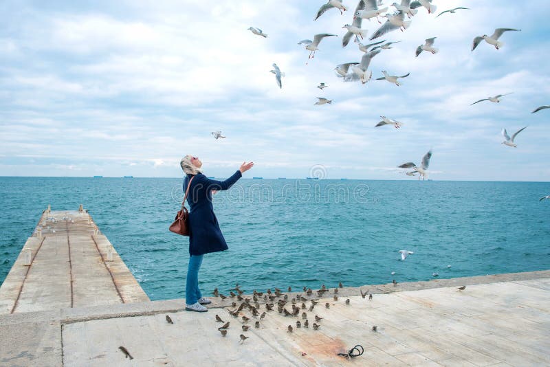 Blonde woman feeding seagulls in cloudy autumn day